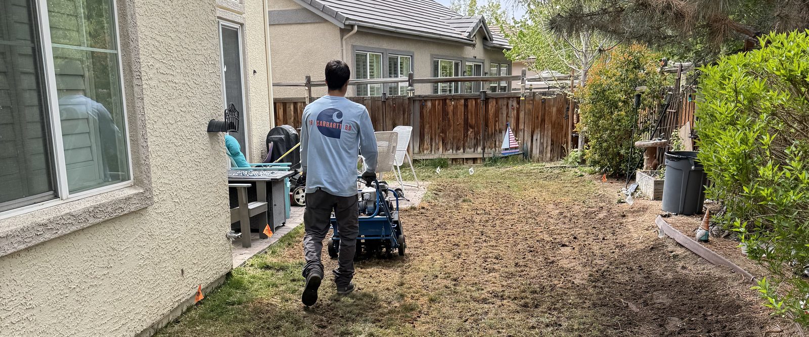 Crew member pushing a core aerator across a backyard lawn for Spanish Springs Lawn Care